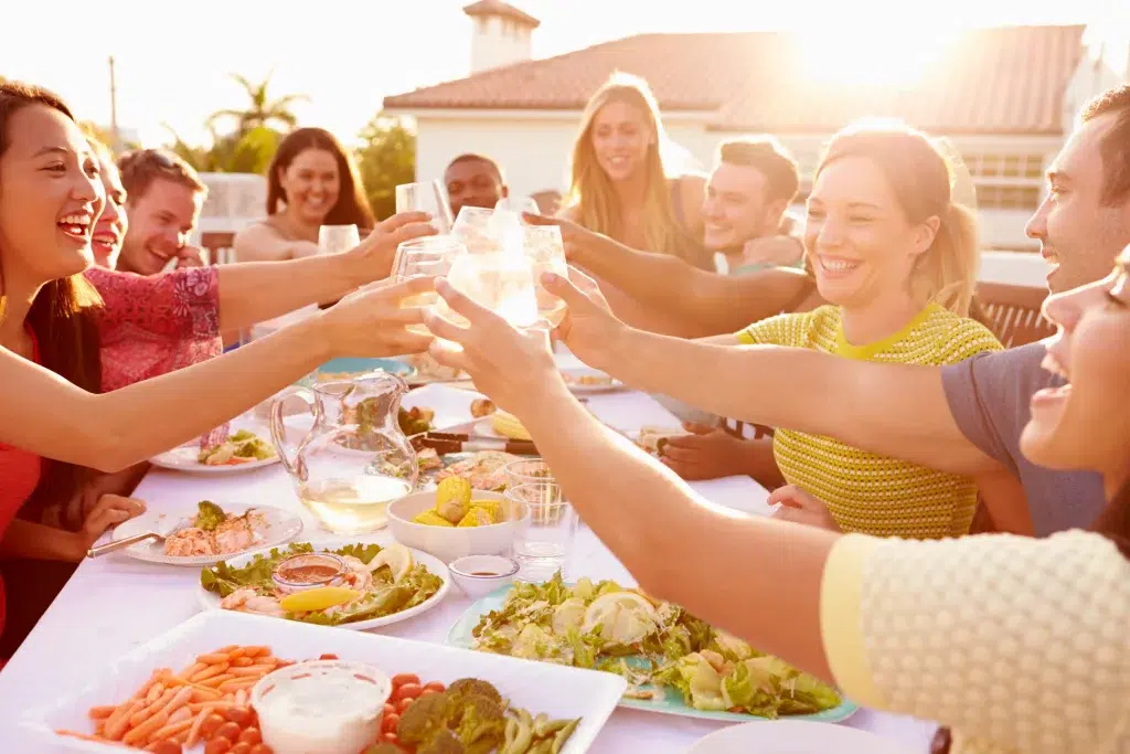 eine Gruppe von Menschen, die an einem Tisch voller Essen auf den Sommer anstoßen